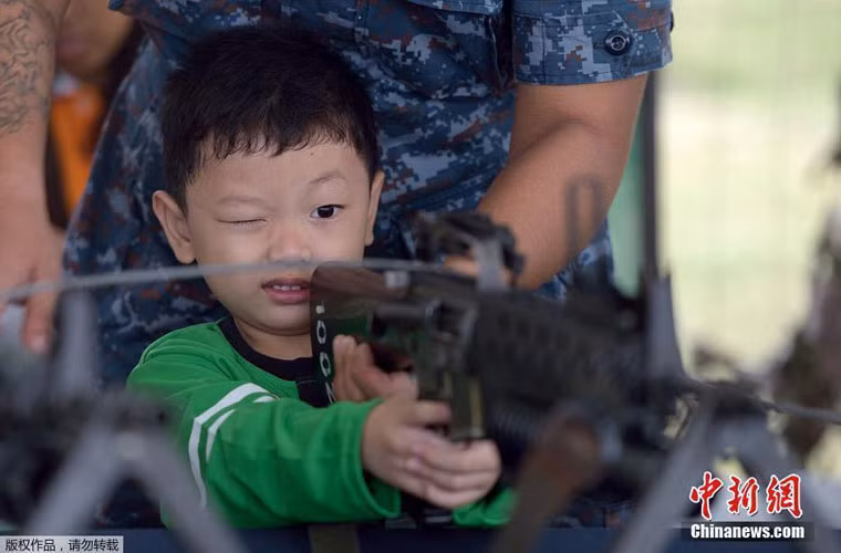 Một em bé thử khẩu súng trường M16 dưới sự hỗ trợ của một binh sĩ.