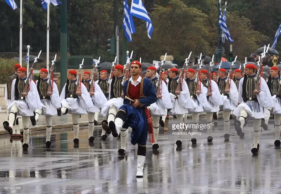 Những binh sĩ Hy Lạp trong trang phục truyền thống sải bước dài trên đường mưa ướt. Mặc dù đất nước đang có nhiều bế tắc về tình hình kinh tế, song việc tổ chức duyệt binh hoành tráng đã thể hiện sức mạnh quân sự và niềm tự hào của Hy Lạp.
