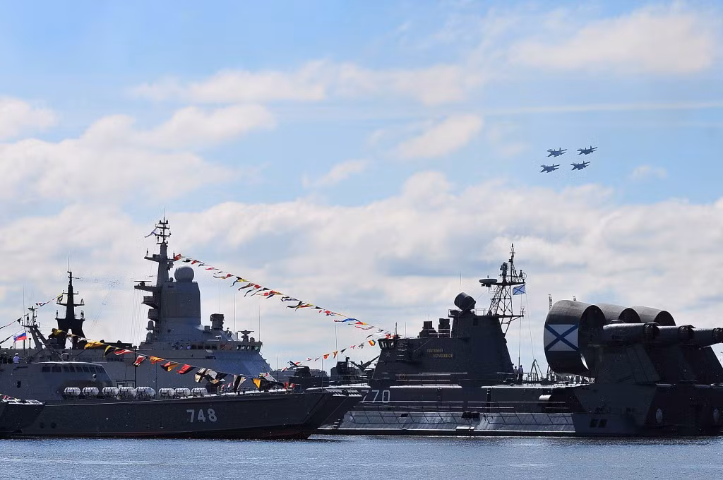 Các tiêm kích MiG-29 đang múa lượn trên không trung. Phía dưới là các chiến hạm Nga đã quần tụ về địa điểm triển lãm vũ khí Hải quân Nga IMDS 2015.