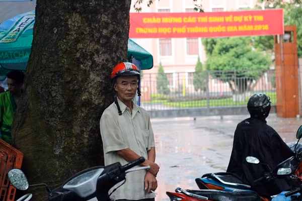 Một phụ huynh không mang theo áo mưa, đứng co ro dưới gốc cây lớn chờ con.