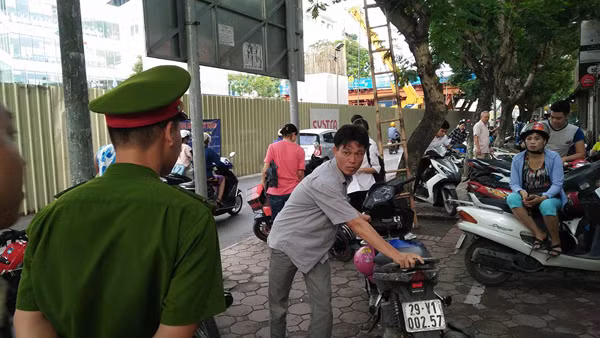 Một chiến sĩ cảnh sát nhắc nhở phụ huynh đưa con đi thi xếp xe gọn gàng để không gây cản trở giao thông. Ảnh chụp tại điểm thi Đại học Sư phạm Hà Nội.