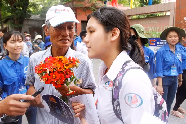 Ông Đức năm nay đã 73 tuổi (ở Hà Đông, Hà Nội) cầm bó hoa mà mình tự làm đến trước cổng trường thi tặng cháu ngoại là Nguyễn Thị Hồng Nhung để động viên tinh thần cháu tiếp tục cố gắng hoàn thành tốt các môn thi còn lại. Em Nhung chia sẻ: "Em làm bài tốt, các câu trong bài đều không khó và có thể đạt điểm giỏi cho bài làm". Ảnh: Mạnh Hưng.