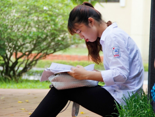 Nữ sinh xinh xắn tranh thủ ngồi bên ngoài ôn lại bài thi trước khi vào phòng. Ảnh: Hưng Bùi.