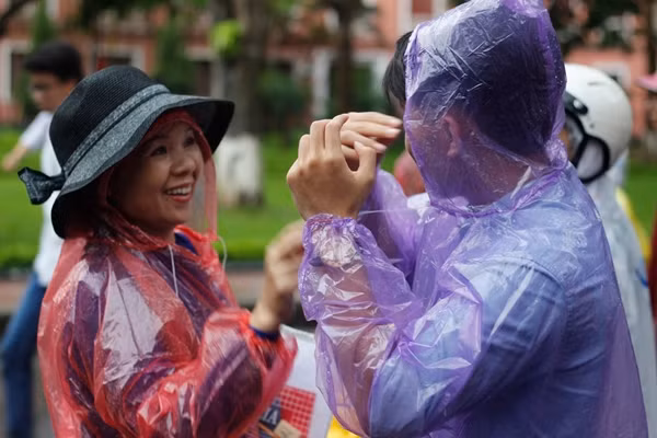 Người mẹ tận tình mặc áo mưa cho cậu con trai sau khi em hoàn thành xuất sắc bài làm của mình.