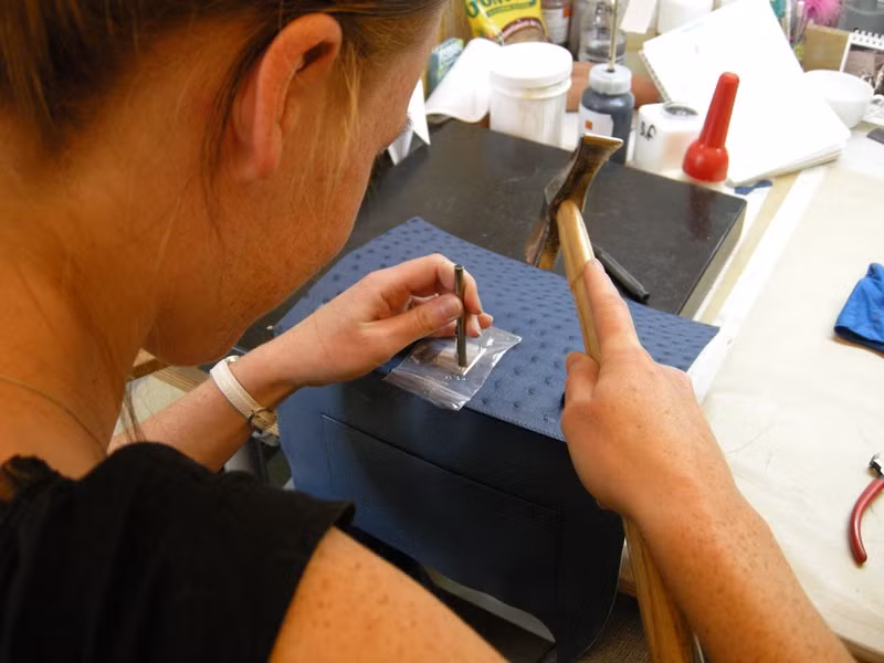 Các phụ kiện của túi Hermes như khóa, chìa khóa, các móc và đinh ghim đều được mạ vàng hoặc bạch kim để tránh bị oxy hóa. Với những dòng túi cao cấp hơn, móc khóa và khóa có thể làm bằng vàng và bạch kim thật. Bên cạnh đó, các tùy chọn bọc da, hoặc gắn nạm kim cương đều được hãng Hermes sẵn sàng chiều lòng các vị khách quý. Trong hình là một người thợ lành nghề đang đóng khóa cho chiếc túi xách da đà điểu tại xưởng của hãng Hermes ở Paris.