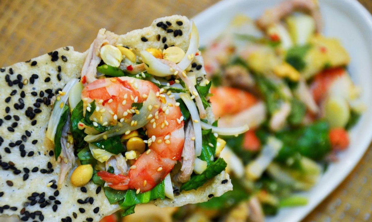 Phần nước trộn gồm nước mắm, đường, chút nước chanh, nêm nếm cho vừa khẩu vị rồi tưới lên đĩa gỏi. Rau thơm, rau răm ta sắt nhỏ ra, đậu phụng rang lên bầm nhỏ ra, bánh phồng tôm xung quanh đĩa. Ảnh: youtube.com.