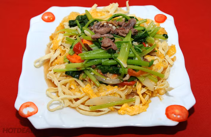 Đợi dầu sôi cho phở vào chiên trước. Tách sợi phở tơi ra. Đợi 5 phút phở bắt đầu giòn. Cho trứng đã đánh lên vào. Đợi giòn hai mặt, bật to lửa r vớt lên cho ráo dầu ăn. Chỉ cần cho phở chiên ở dưới và cho rau xào ở trên vào là hoàn thành. Ảnh: hotdeal.vn.