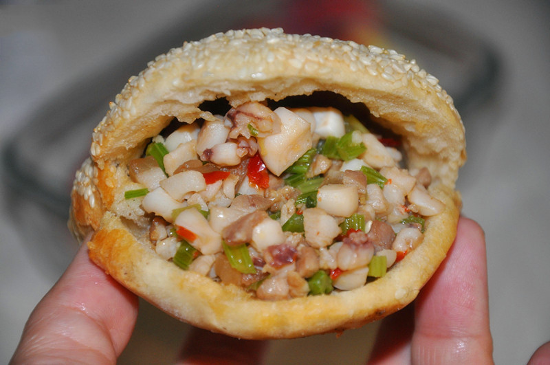 Sau đó dùng vật nặng cán cho từng viên bột tròn lép. Cho chảo dầu lên bếp, đợi dầu sôi cho bánh vào chiên cho đến khi bánh vàng đều các mặt. Đặt bánh lên giấy thấm dầu cho ráo dầu tránh để dầu thấm vào bánh. Xẻ một đường quanh viền bánh tiêu và thêm nhân vào bên trong. Ảnh: TinyBook.net.