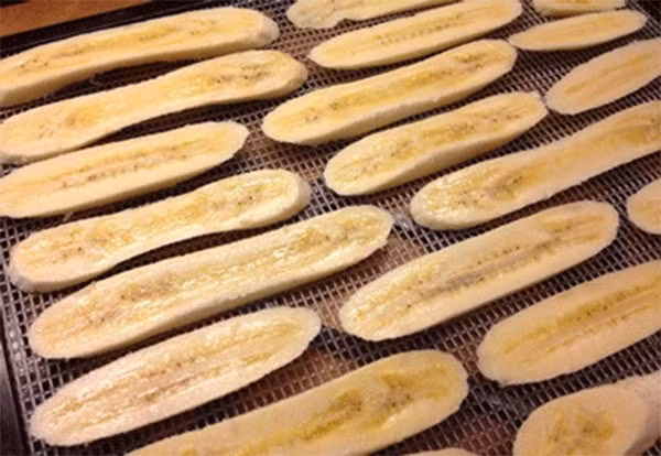 Sau khi xếp chuối vào khay nướng, bạn dùng bình xịt nước chanh pha loãng và xịt lên toàn bộ miếng chuối. Sau khi xịt xong, vẩy đều lớp vani lên bề mặt chuối và đưa vào lò nướng để sấy trong 20 phút ở nhiệt độ khoảng 120 – 125 độ. Ảnh: Emvaobep.com.