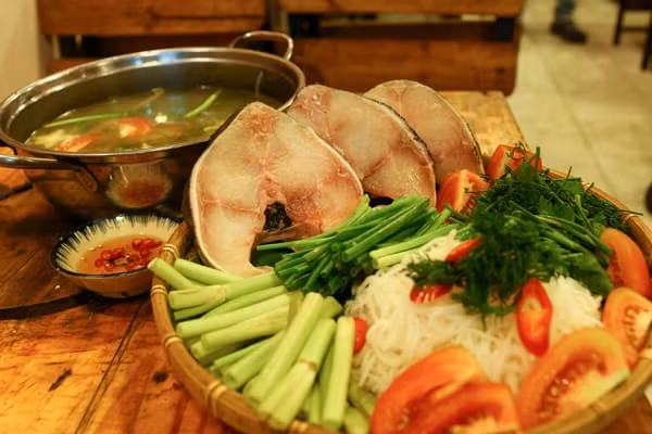 Tắt bếp, thêm thìa nước mắm cho thơm, cho nước lẩu ra nồi lẩu. Rắc chút ngò ôm, ngò gai xắt nhỏ lên trên, thêm vài lát ớt xắt và chỗ tỏi, sả phi thơm chừa lại ở trên là chúng ta đã có nồi nước lẩu thơm ngon. Khi ăn bắc nồi nước lẩu, nước sôi thả cá vào đun khoảng 2 phút cá chín, nhúng các loại rau ăn cùng. Ảnh: hoidaubepaau.com.