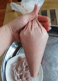 4. Nhồi xúc xích. Để nhồi xúc xích dễ dàng, nên cho nhân thịt vào trong một túi nilon có góc nhọn ở đáy. Sau đó cắt đáy và bóp dần nhân vào vỏ. Ảnh: Emdep.vn