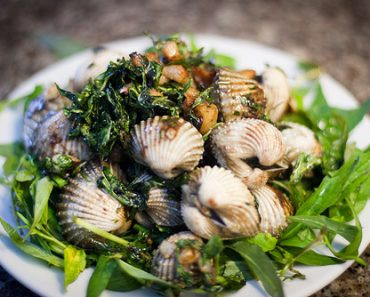 Phi tỏi vàng thơm rồi cho sò huyết vào xào đều lên. Nêm gia vị cho sò thấm đều. Cho nước me đã pha vào rồi nêm nếm lại cho vừa ăn. Cho kiệu vào đảo đều lên. Cho bột năng pha loãng vào để sốt sền sệt lại. Rắc mè rang vàng vào. Tắt bếp. Múc ra đĩa rồi cho lá húng quế xắt nhỏ vào. Ảnh: 7monngonmoingay.vn.