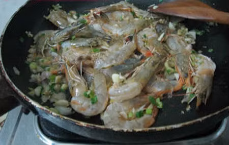 Làm nóng một chảo khác (hoặc nếu tận dụng chảo cũ để xào tiếp thì bạn nên rửa lại để tránh gia vị bị cháy khét không tốt cho sức khỏe) với chút dầu, chờ dầu nóng thì trút hành tây, ớt và cà chua vào xào cùng lúc. Sau đó cho tôm vào đảo đều. Hòa tan hỗn hợp đường, nước cốt chanh, nước mắm trong một bát nhỏ. Từ từ đổ hỗn hợp này vào chảo tôm đang xào, đảo đều. Ảnh: Tinmoi.vn.