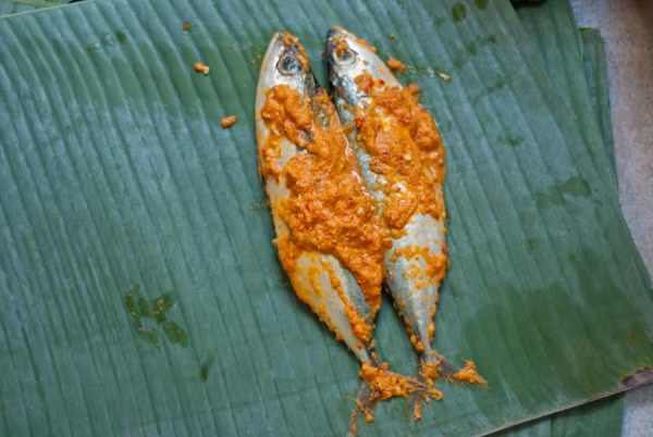 Đặt cá vào lá chuối, lưu ý, nếu gói 1 con cá thì sẽ nướng nhanh hơn nhiều so với việc gói 2 con cá vào một tờ lá chuối. Cuộn tròn cá trong lá chuối rồi dùng tăm xiên để cố định hai đầu lá chuối. Ảnh: Womantoday.vn.