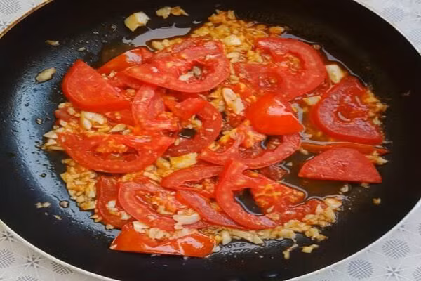 Gạn lấy nước trong để nấu canh. Nặn sạch đầu đen của trai, rửa sạch thái nhỏ ướp với nhánh gừng rửa sạch đập dập băm nhỏ cùng thìa bột nêm. Cho thìa dầu vào phi thơm hành khô cho trai và cà chua vào xào, cho bột nêm đảo đều cho ngấm. Ảnh: monngon.tv.