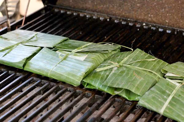 Lá chuối hơ từng miếng qua lửa hoặc phơi ra nắng cho lá mềm mặt, chia thịt bò ra từng phần, bôi qua một lớp dầu mỏng vào mặt trong phiến lá. Sau đó gói từng phần thịt vào mặt lá chuối có bôi dầu thành miếng mỏng cỡ hai ngón tay. Ảnh: TinyBook.vn.