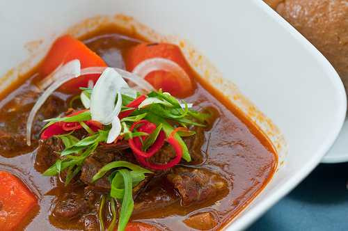 Cho cà rốt, hành tây vào nấu tiếp 15 phút, hòa bột bắp với ít nước lọc, khuấy tan cho vào nồi, nấu thêm 5 phút là hoàn thiện. Làm chén muối ớt chanh, dọn kèm bánh mì, ai thích rau thì ăn kèm ngò gai + húng quế. Ảnh: VTC.vn.