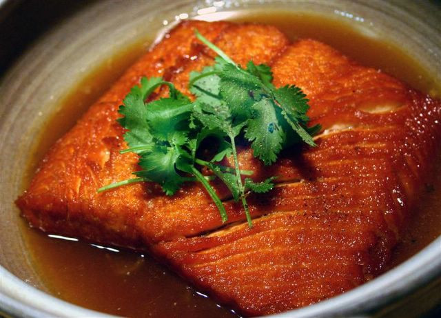 Phi tỏi thơm, cho cá đảo sơ, đảo nhẹ tay kẻo nát cá. Xếp cá hồi vào nồi đất, cho nước dừa đun sôi, gừng, ớt, tiêu xanh, nêm thêm nước mắm, đường cho vừa ăn, lửa nhỏ 30 phút cho thấm cá. Dùng nóng với cơm trắng. Ảnh: cakholangvudai.com.