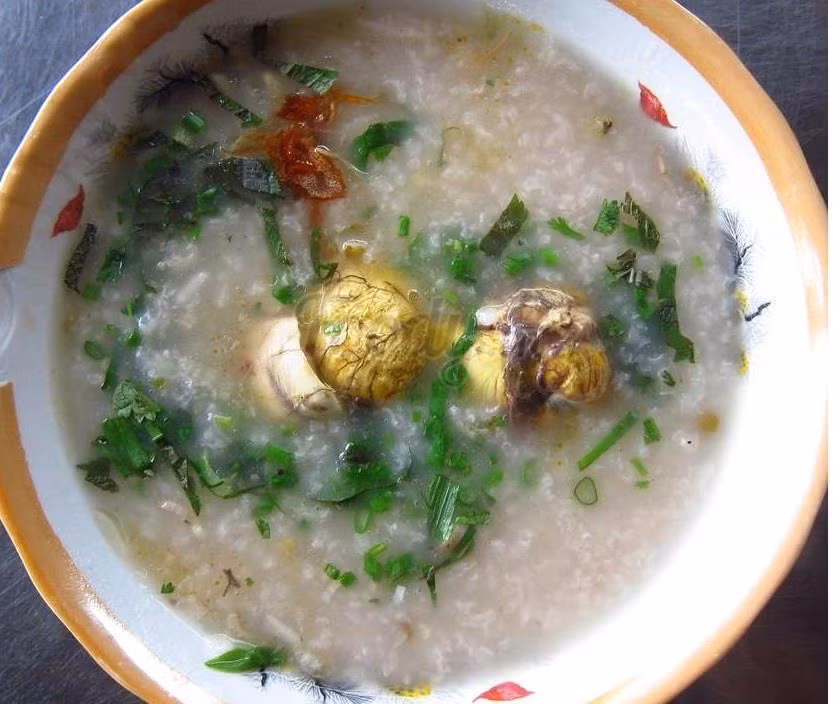 Khi cháo chín, nêm nếm cho vừa ăn, đổ phần nấm rơm vào sau cùng, thêm hành. Tắt bếp. Dùng kèm với rau đắng, thái nhỏ rau răm, rắc thêm chút tiêu. Ảnh: JAMJA.vn.