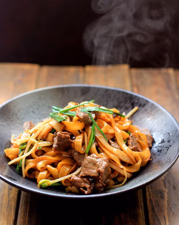 Tiếp sau cho nước, 2 thìa nước tương đen, 2 thìa nước tương vào và đảo đều lên. Sau đó cho bánh phở vào đảo cùng. Xào bánh phở trong khoảng 3 phút để phần bánh phở thấm nước sốt. Thêm thịt bò vào rồi đảo thêm 2 phút nữa thì tắt bếp. Ảnh: beptusomotvietnam.vn.