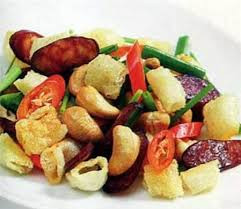 Tỏi đập dập, băm nhỏ, phi trong dầu đến thơm, cho lạp xường vào rán chín, sau đó cho hạt điều, ớt và rượu mai quế lộ, hạt nêm vừa ăn. Cho bóng cá rán và hành vào, đảo nhanh và tắt bếp. Ảnh: Tinbaihay.net.