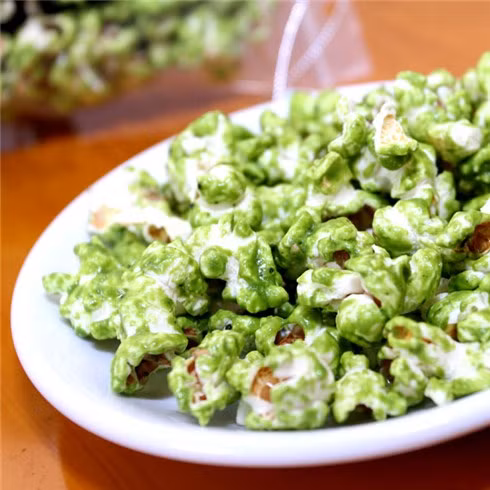 Rây đường xay và bột trà xanh matcha thật mịn, sau đó trộn đều. Khi bắp còn nóng, cho đường xay cùng bột trà xanh vào, đậy nắp hộp, lắc mạnh đến khi hỗn hợp này phủ đều hết tất cả các hạt bắp thì đổ bắp ra khay, để nguội. Ảnh: cungmua.com.