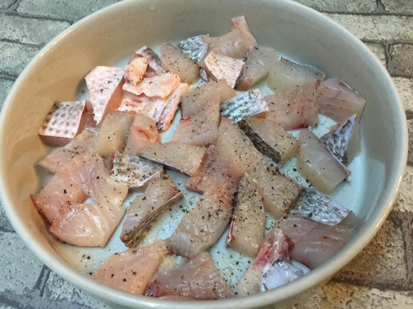 Làm sạch cá, thái thành những miếng vuông vừa ăn. Cho cá vào tô nướng chịu nhiệt, ướp một chút gia vị, rắc thêm hạt tiêu. Rắc tỏi đập dập và tương cà chua lên bề mặt cá. Cà chua rửa sạch, thái khoanh tròn xếp lên trên. Ảnh: Tin247.com.