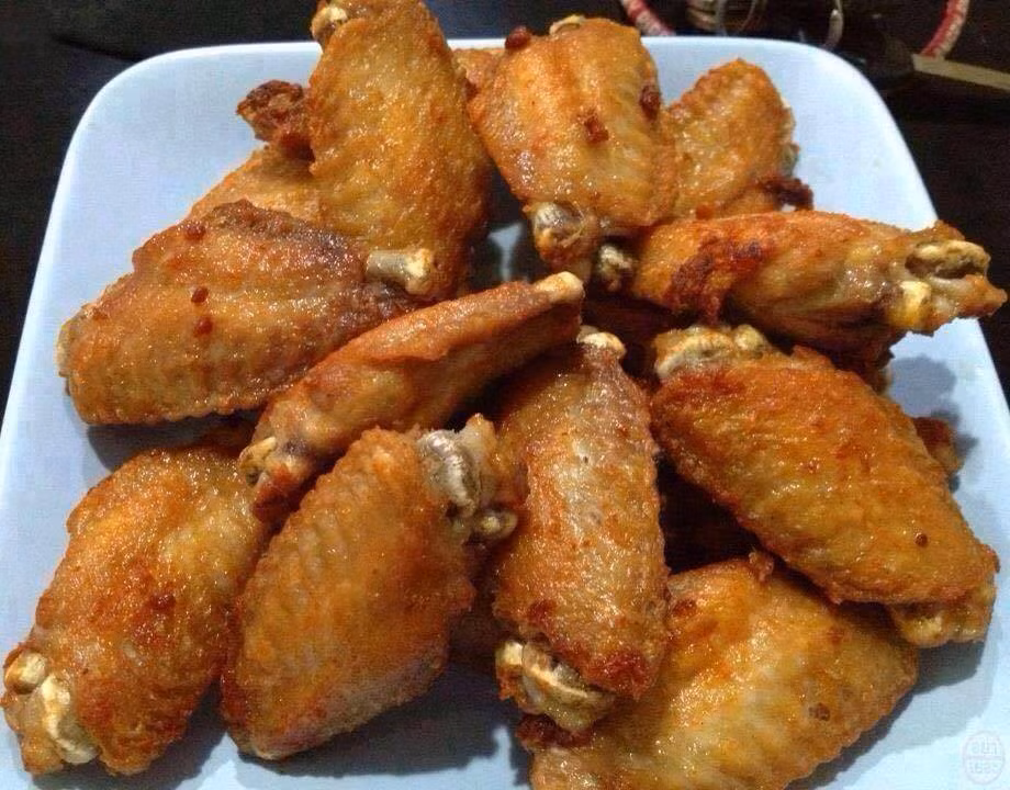 Bơ phi nóng già, cho hạt tiêu xay, muối, mì chính rồi rưới đều vào cánh gà. Cà chua 1 quả tỉa hoa, 1 quả thái mỏng. Xà lách rửa sạch ngâm qua nước muối loãng, vớt ra để ráo. Xếp cánh gà ra đĩa, xen kẽ dưa chua, cà chua, xà lách, ớt tỉa hoa, rau mùi. Ăn nóng. Ảnh: niemdamme.com.vn.