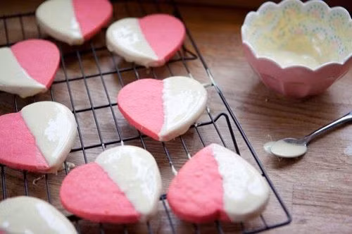 Lấy bột ra, rải đường cát màu hồng lên, cán mỏng và dùng khuôn trái tim cắt bánh. Dùng thìa múc kẹo sữa vào một nửa trái tim, xếp bánh vào khay và nướng khoảng 15 phút. Khi bánh chín, lấy ra thưởng thức và có thể gói lại để tặng người thương. Ảnh: blog.beemart.vn.