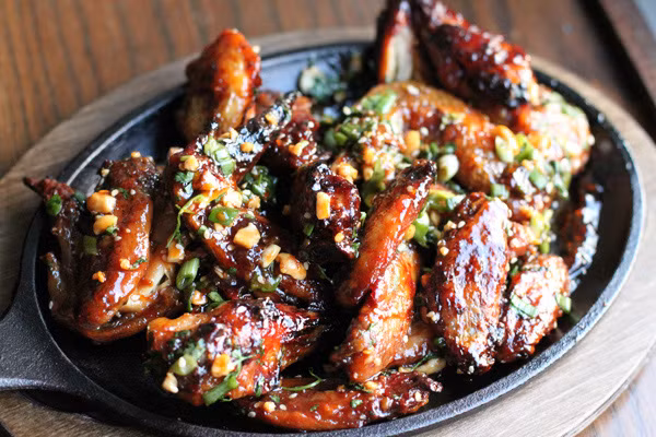 Lấy gà ra khỏi lò. Đổ phần nước sốt ra bát lớn. Cho gà vào, đảo đều để nước sốt bám khắp gà. Sau đó cho gà ngược trở lại vào lò nướng thêm 10 phút nữa. Cho đậu phộng rang, hành lá, rau mùi tây xắt nhỏ vào bát trộn gà lúc trước, trộn đều. Lấy gà ra khỏi lò, rắc phần hành và đậu phộng bên trên vào là xong. Ảnh: aFamily.vn.