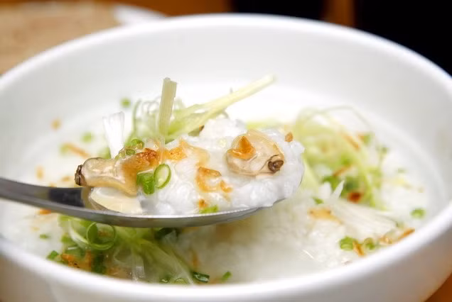 Sau đó, đun nóng dầu ăn phi thơm hành khô xắt lát nhỏ. Khi hành chín, trút hành ra đĩa để nguội rồi cho phần thịt ngao vào xào săn, thịt ngao để ăn với cháo nên xào hơi mặn một chút. Hành lá, rau răm rửa sạch thái nhỏ. Múc cháo chín ra bát, rắc hành lá, rau răm, hành phi, thêm thịt ngao xào săn, rắc tiêu, ớt bột và thưởng thức. Ảnh: homnayangi.vn.