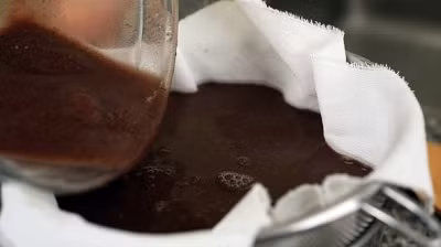 Thêm 2 – 3 cup nước vào, lọc đậu đỏ qua rây, dùng thìa ấn xuống để chiết lấy nước. Đặt 1 miếng vải xô vào lòng rây, đổ nước đậu đỏ vào, đợi vài phút cho nước chảy xuống bát. Túm chặt miếng vải lại và bóp lấy phần nước đậu còn sót lại. Cho bã đậu vào nồi, thêm đường, muối, vani vào, khuấy đều khoảng 3 – 5 phút. Ảnh: kenh14.vn.