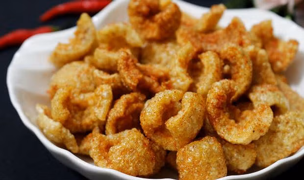 Đun sôi dầu ăn rồi hạ thật nhỏ lửa, thả từng ít bì lợn vào chiên phồng rộp lên rồi vớt ra giấy thấm dầu. Cho bì lợn vào hộp hoặc túi zip xóc thêm xíu bột canh, đường, ớt bột rồi thưởng thức. Ảnh: Baophapluat.vn.