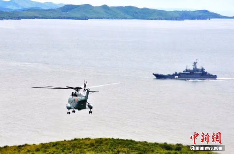 Trực thăng hải quân Z-8 Trung Quốc bay trên hòn đảo mục tiêu, xa xa là tàu Nga.