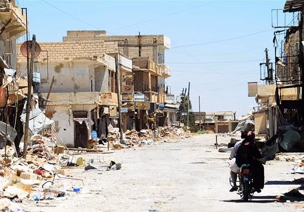 Người dân đi xe máy qua đống đổ nát bên đường ở khu vực phía đông thành phố Aleppo. Ảnh: FNA.