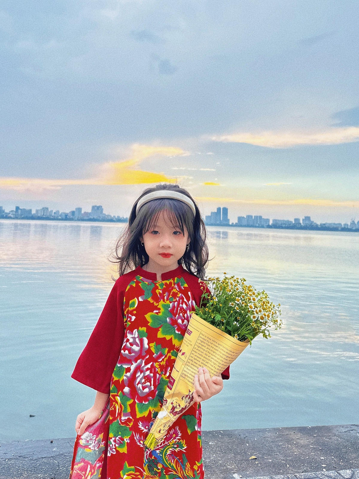 Cô bé được diện cho chiếc áo dài họa tiết chăn con công nổi bật, đeo bờm dịu dàng, ôm bó hoa cúc tana. Ảnh: Vietnamnet