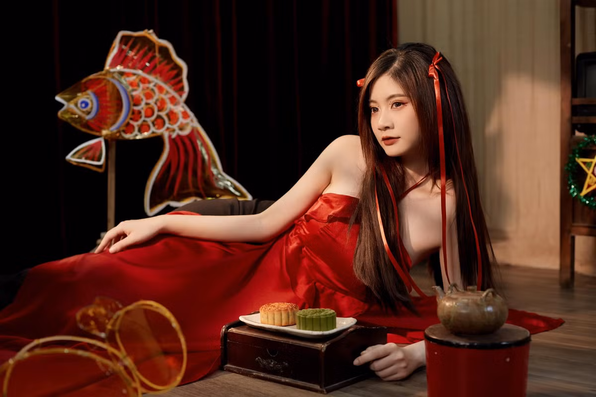 Trong bộ ảnh này, "hot girl má lúm" diện váy yếm màu đỏ, tạo dáng trong khung cảnh đậm chất truyền thống mùa Trung thu là những chiếc bánh, ấm trà và đèn lồng con cá chép,...