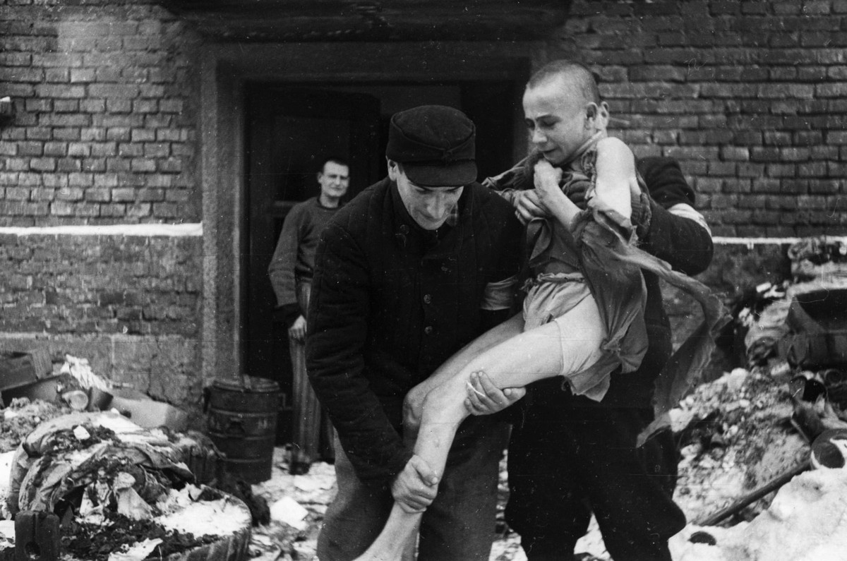Thiếu niên người Liên Xô Ivan Dudnik, 15 tuổi, gầy gò ốm yếu sau nhiều năm bị giam giữ và tra tấn tại trại tử thần Auschwitz. Khi được giải cứu, một số người hỗ trợ đưa Dudnik ra ngoài bởi sức khỏe của em không thể tự đi lại.