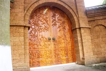 Chiếc cổng độc đáo làm tăng thêm vẻ đẹp cho ngôi nhà khi nó được xây dựng hoàn toàn bằng đá ong, cánh cổng cũng được làm bằng gỗ mít chạm khắc tinh xảo. Ảnh: Vietnamnet.