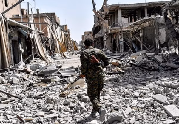 Chiến binh SDF đi qua con đường ngổn ngang gạch đá ở Raqqa. Ảnh: FNA.