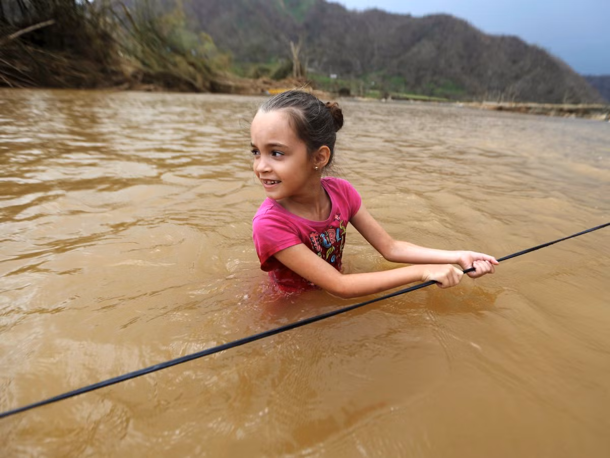 Siêu bão Maria mạnh cấp 4 đã tàn phá Puerto Rico vào ngày 20/9 và gây ra cuộc khủng hoảng nhân đạo tại hòn đảo này. Do ảnh hưởng của bão, cho đến nay phần lớn Puerto Rico bị mất điện. Ngoài ra, thực phẩm, nước uống và nhiều mặt hàng cần thiết khác đều khan hiếm. Ảnh: Bé Ruby Rodriguez (8 tuổi) lội qua sông ở Morovis. Ảnh: BI.