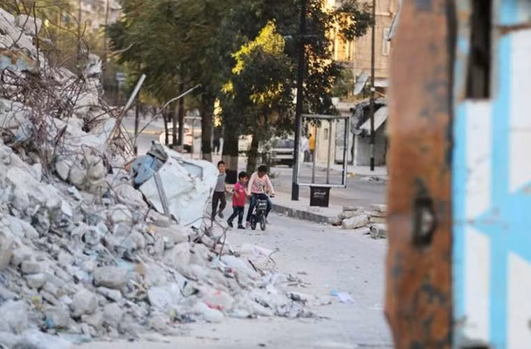 Ba bé trai tập đi xe đạp gần đống đổ nát của những tòa nhà.