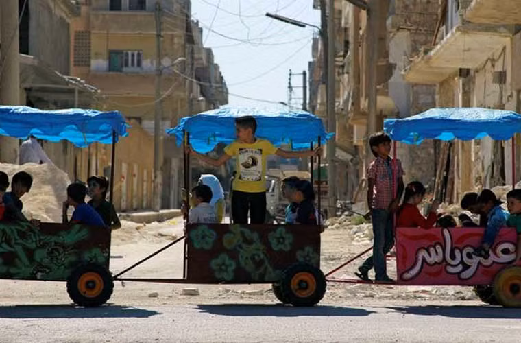 Các em nhỏ Syria ngồi trên xe đi ngang qua phố ở Idlib.