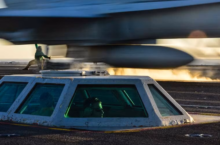 Bức ảnh chụp những người thực hiện ấn nút khởi động máy phóng thủy lực bắn máy bay tiêm kích hạm trên tàu sân bay USS John C. Stennis (CVN-74). Họ có thể được ví như là xạ thủ của cây cung khổng lồ bắn mũi tên tiêm kích hạm lên trời tấn công mục tiêu.