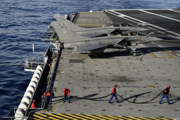 Các kỹ thuật viên đang làm việc cạnh các máy bay Rafale gần đường băng trên tàu sân bay.