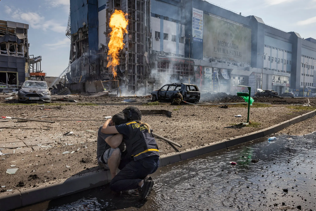 Trong bức ảnh, một nhân viên cứu hộ đang an ủi một người sống sót sau cuộc tấn công bằng tên lửa của Nga vào bãi đỗ xe của một cửa hàng ở Kharkiv.