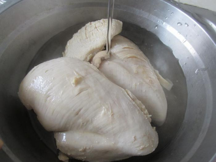 Bước 1: Ức gà cho vào nồi nước lạnh, thêm rượu nấu ăn cùng hành lá và gừng thái chỉ vào đun trong 20 phút. Khi ức gà chín vớt ra ngâm với nước lạnh (nước sôi để nguội) để làm tăng vị ngon của gà.