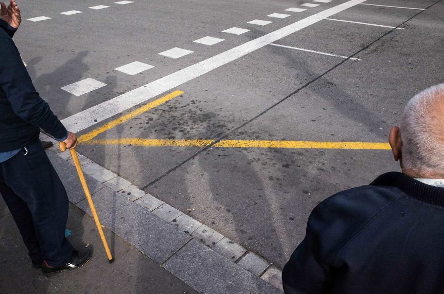 Chiếc gậy màu vàng của người đàn ông vô tình trùng khớp với vạch kẻ đường, tạo thành một hình mũi tên nổi bật.