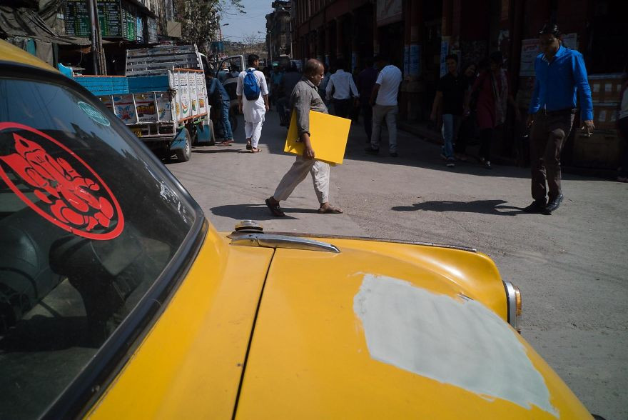 Khoảnh khắc trùng hợp khó tin khi chiếc xe ô tô màu vàng xước sơn đúng một khoảng bằng tấm bảng của người đàn ông đi phía xa đang cầm.