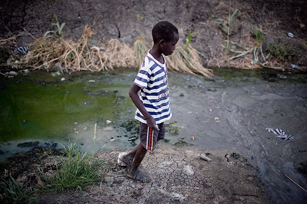 Một bé trai đi bộ qua dòng nước bẩn ở Nam Sudan.